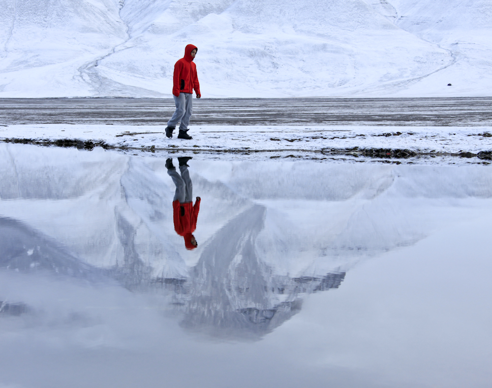 A person walking by the water and it`s reflcetion, mountain also reflected on the water, snowy scenario